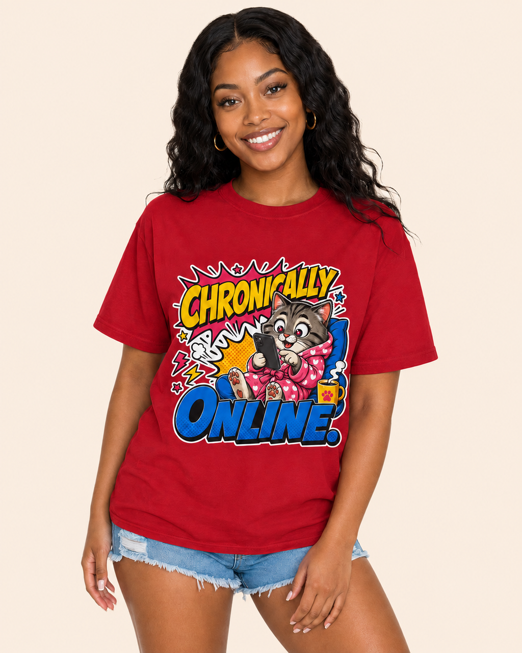 A woman wearing a red graphic t-shirt with a cartoon cat and the text 'CHRONICALLY ONLINE' in comic-style lettering, paired with denim shorts, against a solid beige background.
