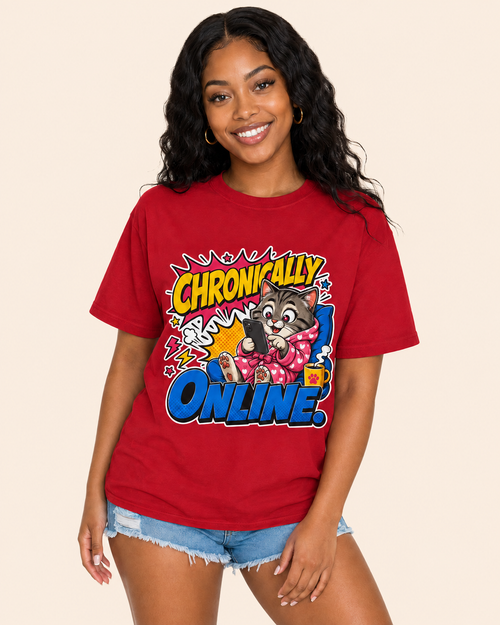 A woman wearing a red graphic t-shirt with a cartoon cat and the text 'CHRONICALLY ONLINE' in comic-style lettering, paired with denim shorts, against a solid beige background.
