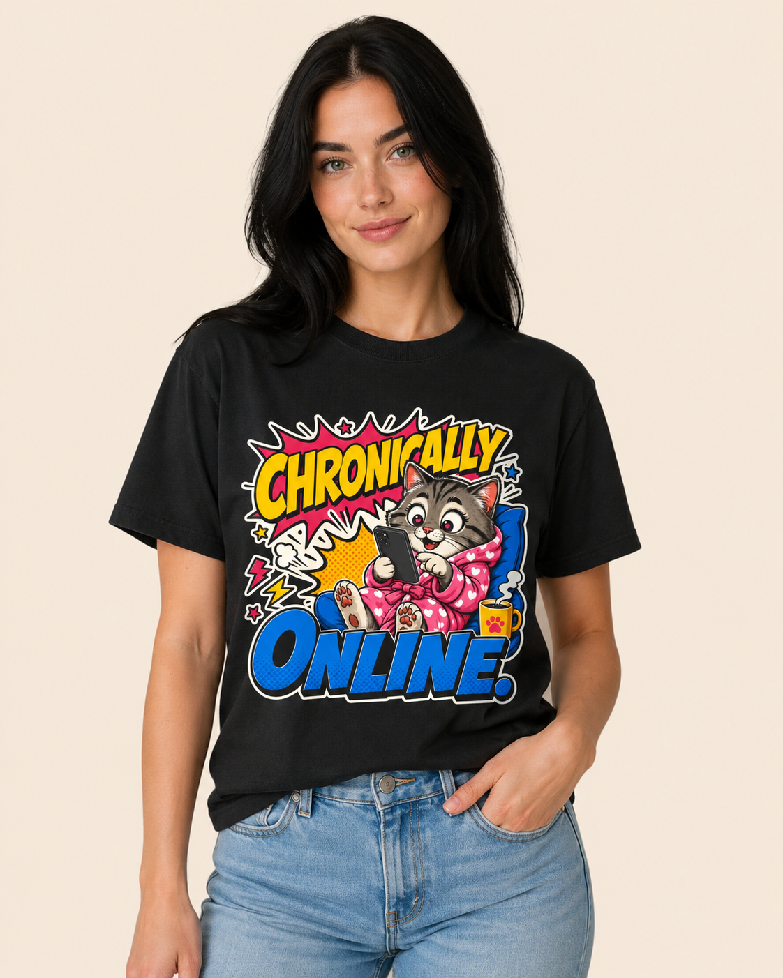 A woman wearing a black graphic t-shirt with a colorful cartoon cat design and the text 'Chronically Online' in comic-style lettering, paired with light blue jeans, set against a solid beige background.