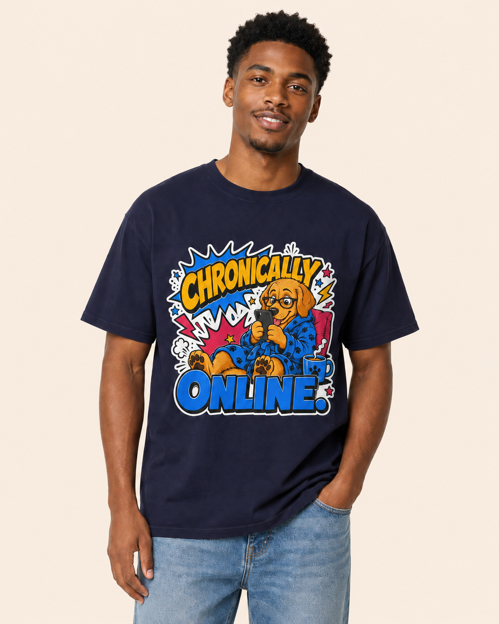 A man wearing a navy blue graphic t-shirt with a cartoon dog and the text 'Chronically Online' in comic-style lettering, paired with light wash blue jeans, set against a solid beige background.