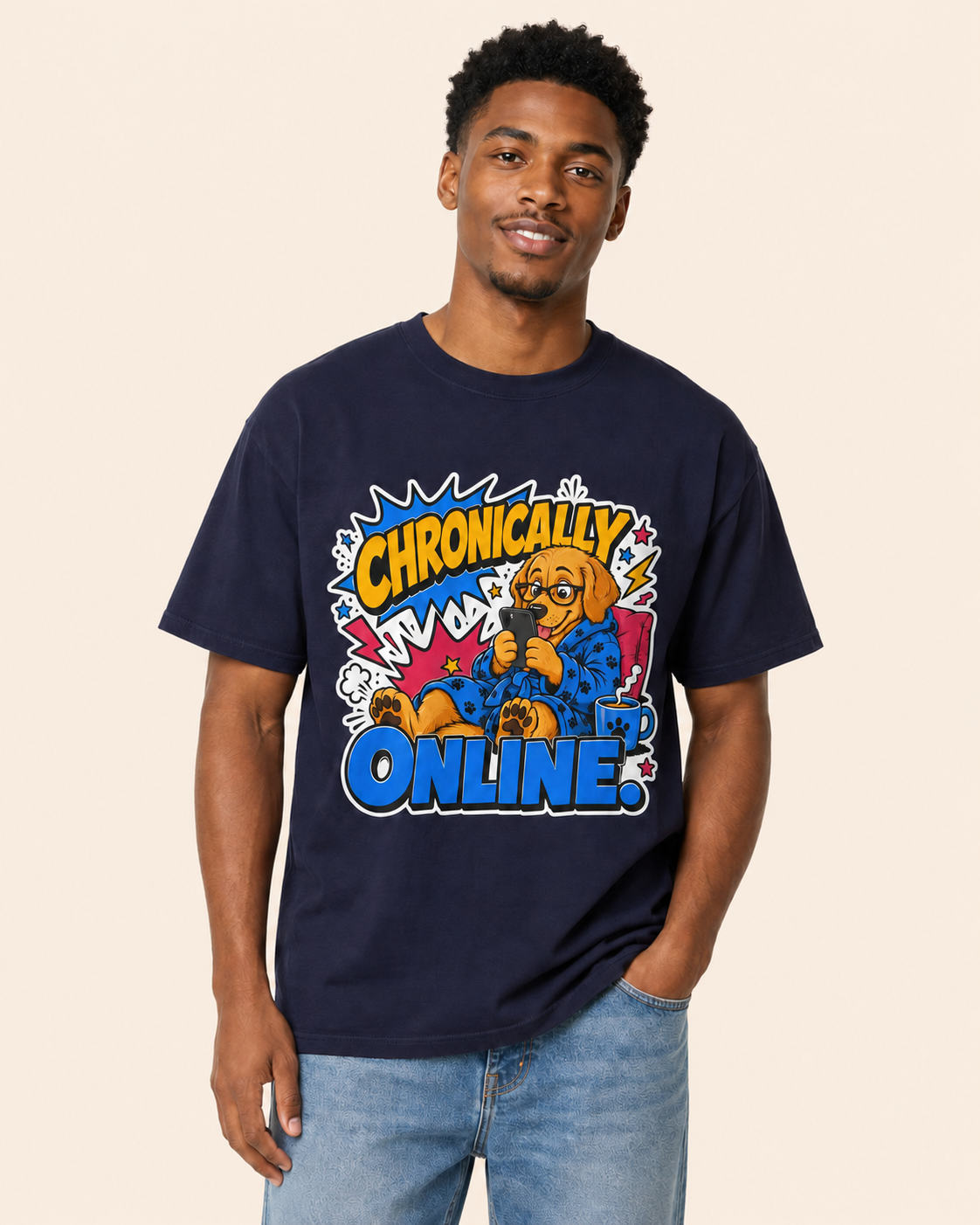 A man wearing a navy blue graphic t-shirt with a cartoon dog and the text 'Chronically Online' in comic-style lettering, paired with light wash blue jeans, set against a solid beige background.